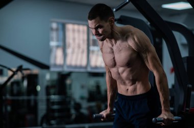Shirtless man doing triceps dips from parallel bars in gym
