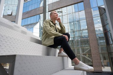 İşitme cihazı olan düşünceli beyaz adam şehir merkezindeki merdivenlerde oturuyor.