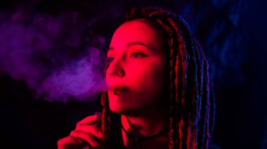 Rastalı beyaz kız kırmızı ışıkta sigara içiyor.