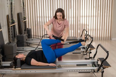 Aşırı kilolu beyaz kadın kişisel antrenörle pilates egzersizi yapıyor.