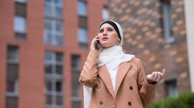 Açık havada akıllı telefondan konuşan tesettürlü genç kadın.