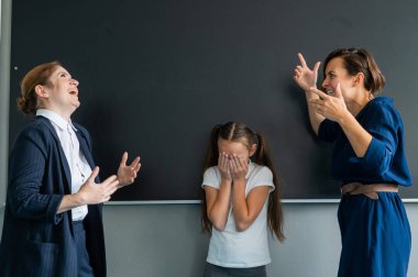 Bir bayan öğretmen ve bir öğrenci anne birbirlerine tahtada bağırıyorlar. Liseli kız ağlıyor.