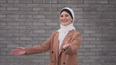 Mavi gözlü genç bir kadının portresi gri tuğla bir duvara karşı tesettürlü.