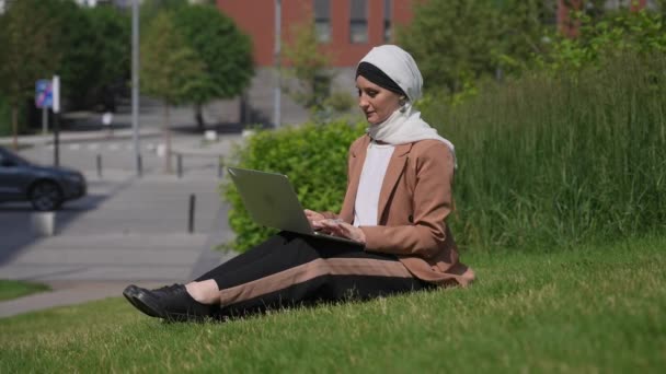 Młoda Kobieta Hidżabie Siedzi Trawniku Używa Laptopa Zewnątrz Pokazuje Kciuki — Wideo stockowe