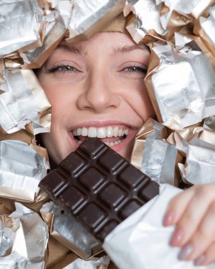 The face of a Caucasian woman surrounded by candy wrappers. The girl eats a bar of chocolate