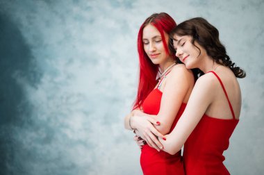 Aynı kırmızı elbiseleri giymiş şefkatle sarılan iki kadının yakın plan portresi. Lezbiyen samimiyeti