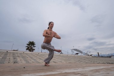 Beyaz bir adam, çıplak gövdesiyle deniz kıyısında wushu yapıyor.