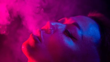 Kısa saçlı Asyalı kadın neon ışıkta sigara içiyor. yakın plan portre
