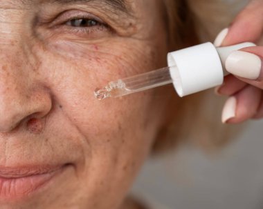Pipetle hyaluronik asit serumu uygulayan yaşlı bir kadının yakın plan portresi. Yaşlanma karşıtı yüz bakımı