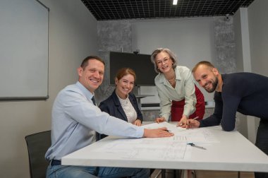 Tasarımcılar bir toplantıda çizimleri tartışırlar. Dört gülümseyen iş adamı kameraya bakıyor.