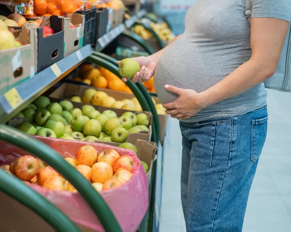 Pregnant woman chooses apples in the store