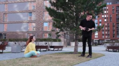 Beyaz kadın çimlerin üzerinde otururken poz veriyor. Bir adam bir mankenin fotoğrafını çeker ve takla atar.