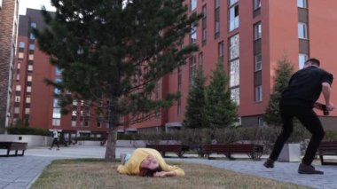 Beyaz kadın çimlerin üzerinde yatıyor. Adam onun üzerinde takla atıyor ve fotoğraf çekiyor.