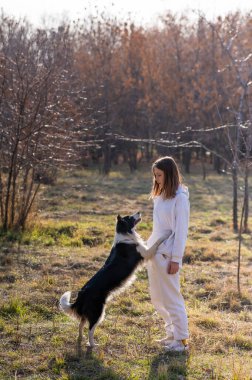 Beyaz kadın sonbahar parkında bankta otururken köpeğine sarılıyor.