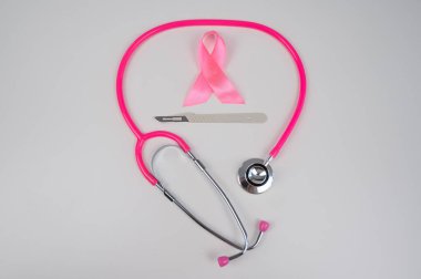 Beyaz arkaplanda pembe stetofonendoskop, saten kurdele ve neşter.