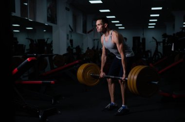 Kafkasyalı bir adam spor salonunda dambıllarla kol egzersizi yapıyor.