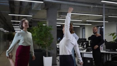 Four office workers warm up during a break. Employees do fitness exercises at the workplace. Slow motion