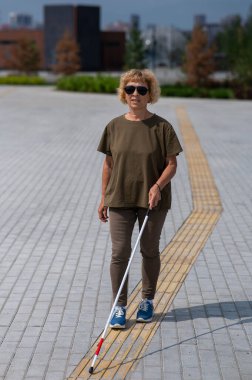 Yaşlı bir kör kadın, değnekle dokunmatik bir şekilde yürür.
