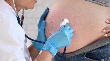 Doktor hamile bir kadının bebeğinin kalp atışlarını dinler.