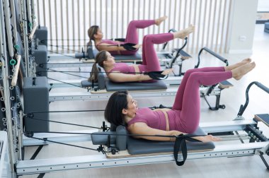 Pembe spor kıyafetli üç Asyalı kadın ıslah yatağıyla pilates egzersizi yapıyor.