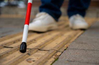 Kör bir kadın, sarı kiremitler üzerinde sokakta yürüyor. Dokunsal bastona odaklan.