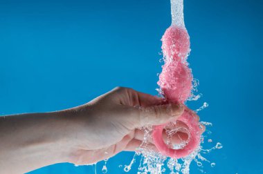 Mavi arka planda akan suyun altında pembe anal boncuklar tutan bir kadın. Seks oyuncağı hijyen konsepti