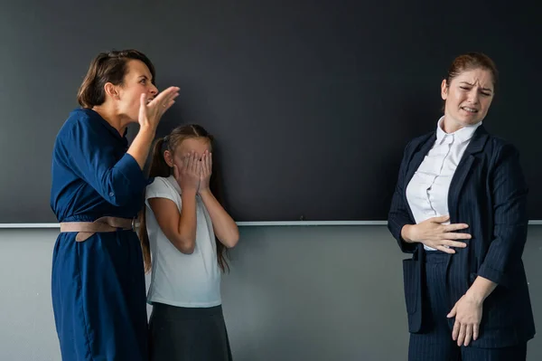 Schoolgirl and her mother yell at the teacher standing at the blackboard