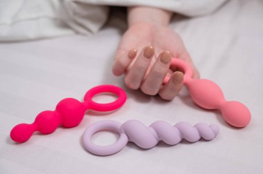 Bir kadın yatakta yatarken bir setten anal boncuk seçer.