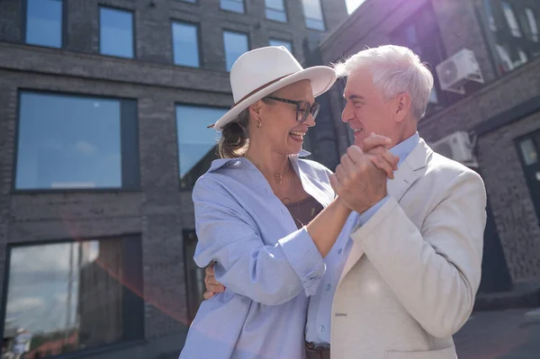 An elderly couple in love dances outdoors. A gray-haired man and a mature woman laugh and hug