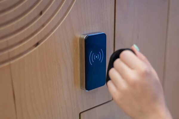 A woman opens the electronic lock of a cubicle in a locker room with a bracelet