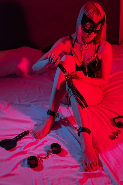 一个戴着脚镣的女人躺在霓虹灯下的床上 Bdsm概念 — 图库照片
