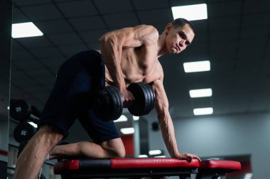 Gömleksiz bir adam spor salonunda dambıl sırasına dizer.