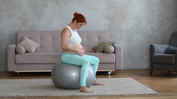 Mujer Embarazada Pelirroja Acariciando Vientre Mientras Está Sentada Una Pelota — Vídeos de Stock