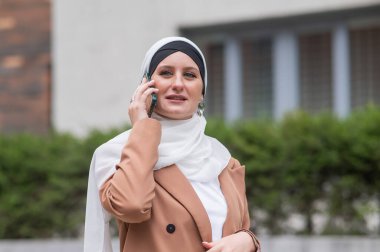 Açık havada akıllı telefondan konuşan tesettürlü genç kadın.