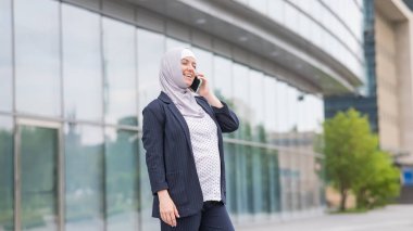 Başörtülü ve takım elbiseli hamile iş kadını akıllı telefondan konuşuyor.