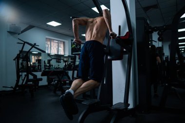 Shirtless man doing triceps dips from parallel bars in gym