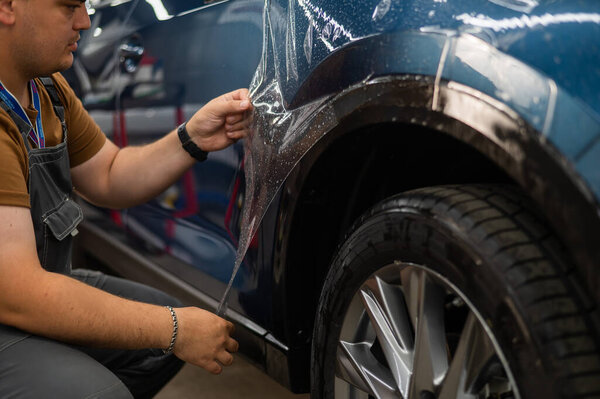 The master in the car service applies a protective armor film to the car body