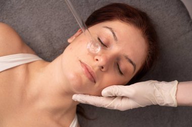 Doktor, kadın bir hastanın yüzündeki sivilce için darsonval aparatı kullanıyor.