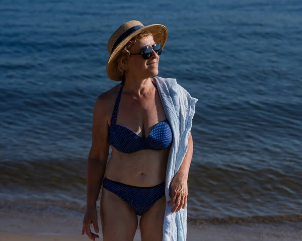 一位戴着草帽 太阳镜和泳衣的老妇人正在海滩上休息 — 图库照片
