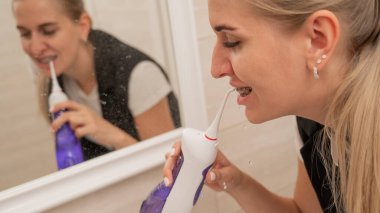 Dişlerinde diş teli olan bir kadın sulayıcı kullanır. Yakın plan portre