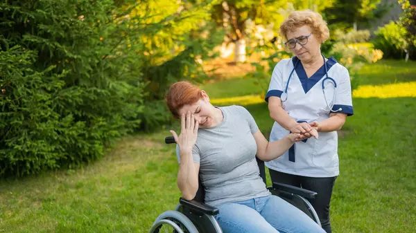 Elderly nurse comforting woman sitting in wheelchair outdoors