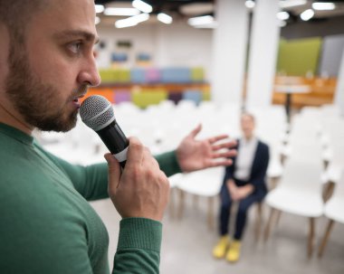 Kızıl saçlı beyaz bir iş kadını boş bir konferans odasının ön sırasında oturuyor. Sakallı adam ders veriyor.