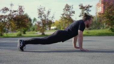 Uzun saçlı sakallı adam spor sahasında şınav çekiyor.