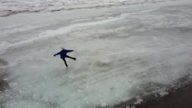 Donmuş bir gölde mavi kazak giyen bir kadının hava görüntüsü. Artistik patinajcı programı gerçekleştirir