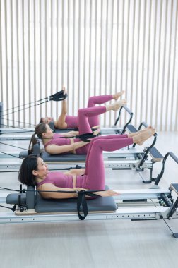 Pembe spor kıyafetli üç Asyalı kadın ıslah yatağıyla pilates egzersizi yapıyor.