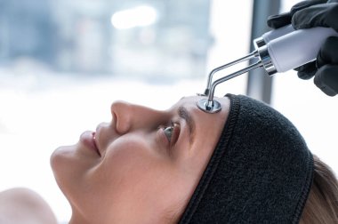 Genç beyaz kadın mikro akım terapi prosedürü uyguluyor. Güzellik bürosu