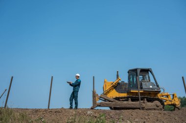 İnşaat alanında elinde dizüstü bilgisayar tutan beyaz erkek müteahhit.