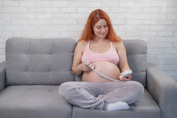 Rudowłosa Kobieta Ciąży Siedzi Kanapie Używa Domowego Dopplera — Zdjęcie stockowe