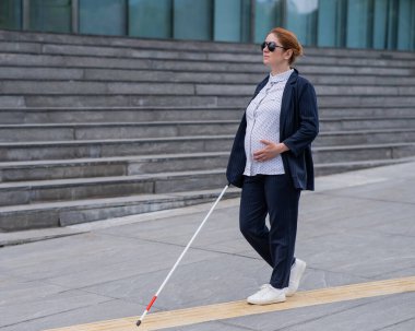 Kör hamile iş kadını bastonuyla dokunsal fayanslar üzerinde yürüyor.