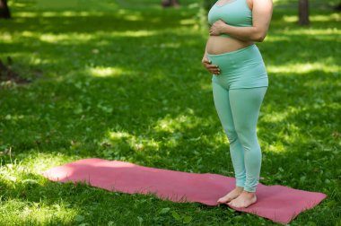 Dışarıda yoga yapan hamile bir kadının göbeğini kapatın.
